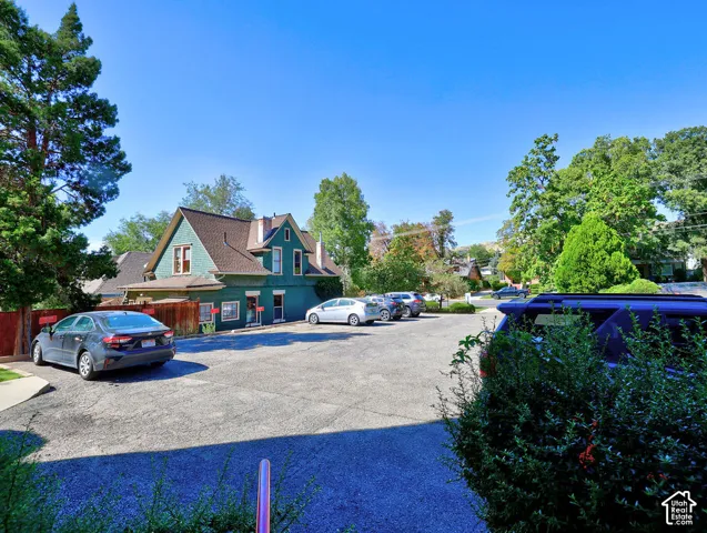 Asphalt parking area with multiple designated spaces, mature landscaping, and an exterior featuring dark green siding and a pitched shingle roof