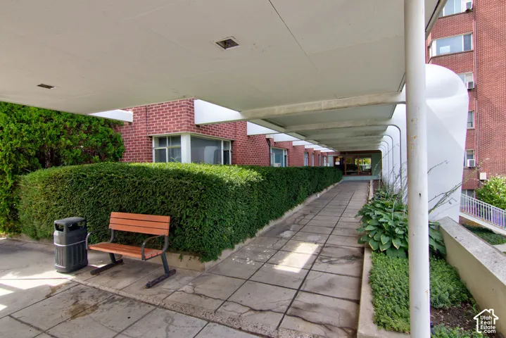 Covered exterior walkway featuring a red brick facade, structural white columns, overhead lighting, and concrete paving