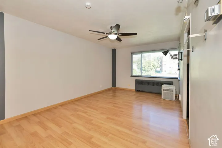 Wood-finish flooring, ceiling fan with integrated lighting, large picture window, and metal radiator unit