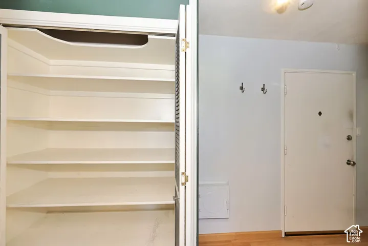 Built-in storage closet featuring five tiered shelves, paired with a solid-panel door and two wall-mounted metal hooks