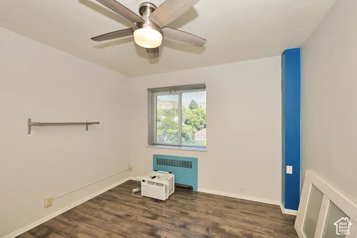 Room featuring wood-finish flooring, a multi-blade ceiling fan with integrated light fixture, a horizontal wall-mounted bar, and a sliding window with horizontal blinds