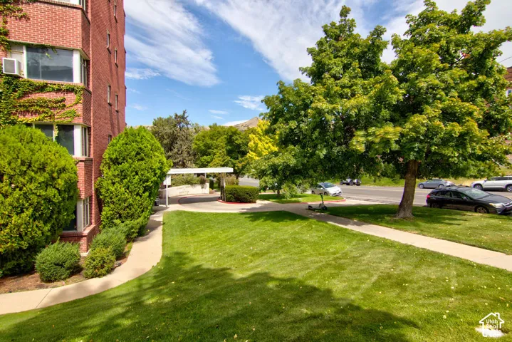 Multi-story brick exterior featuring climbing ivy, expansive manicured lawn, mature shade trees, and concrete pedestrian pathways