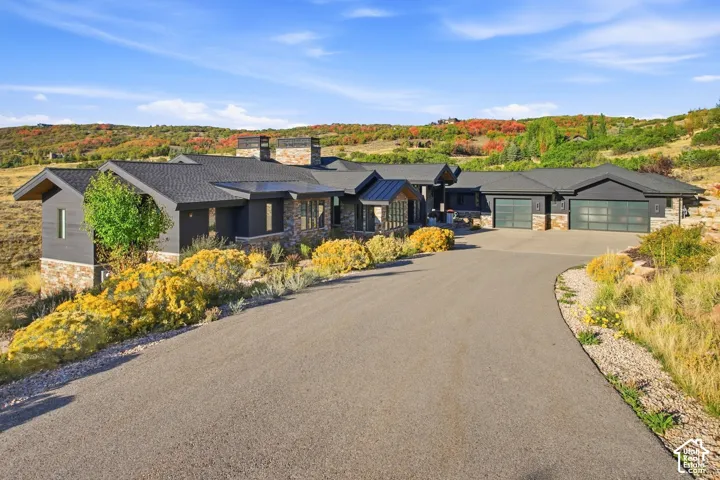 Contemporary architectural exterior featuring stone masonry accents, dark horizontal siding, metal roofing, multiple chimneys, and a multi-car garage