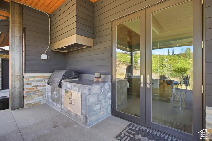 Covered patio featuring an outdoor kitchen with stone masonry, stainless steel cabinetry, a built-in stainless steel ventilation hood, and full-height glass double doors