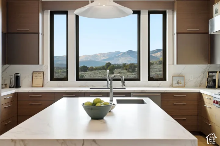 Kitchen featuring flat-panel wood cabinetry, large stone-finish countertops, waterfall-edge center island, undermount sink with arched faucet, and floor-to-ceiling windows with mountain scenery