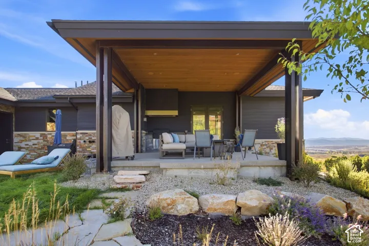 Covered outdoor patio featuring a wood-paneled ceiling, stone masonry foundation, built-in wall-mounted outdoor hood, and flagstone landscaping
