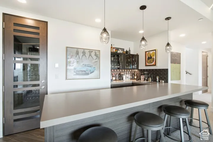 Wet bar featuring a stone-finish countertop, dark wood-finish cabinetry, patterned backsplash tile, glass-fronted upper cabinets, and three glass pendant lights