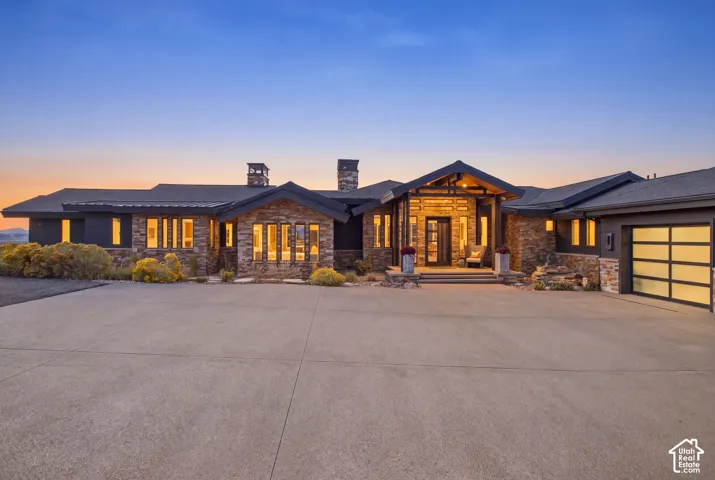 Contemporary exterior featuring multi-tonal stone masonry, dark metal roof accents, expansive concrete motor court, and an integrated garage with translucent panel doors