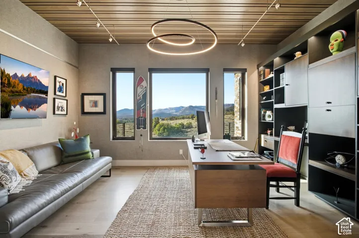 Tongue-and-groove wood-plank ceiling featuring track lighting and a contemporary circular LED fixture, floor-to-ceiling built-in shelving, wood-finish flooring, and expansive windows showcasing mountain scenery