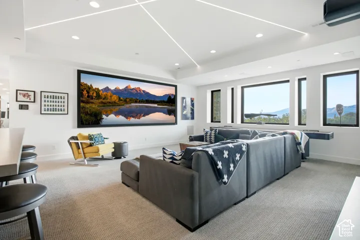 Tray ceiling with integrated linear LED lighting, recessed ceiling lights, large-format wall-mounted screen, floor-to-ceiling windows, and built-in stone-surface counter