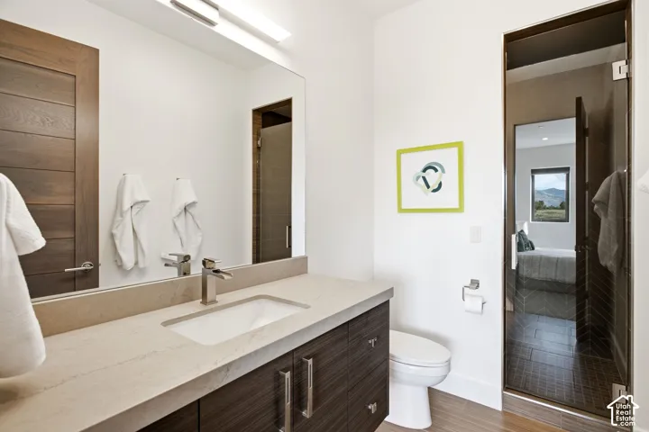 Modern vanity featuring a stone-composite countertop, undermount sink, and wood-finish cabinetry, paired with a full-width vanity mirror and a glass-enclosed shower with tiled interior