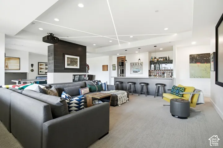 Tray ceiling with integrated linear LED lighting, recessed ceiling lights, built-in wet bar with dark cabinetry, and floor-to-ceiling dark-toned fireplace column