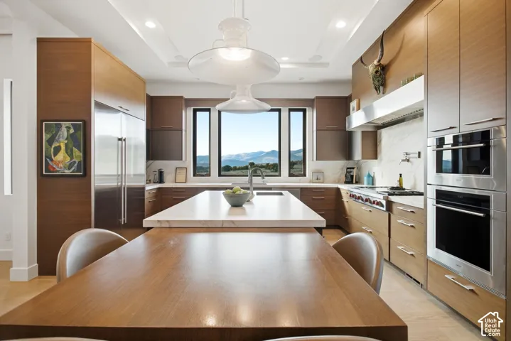 Kitchen featuring horizontal grain wood cabinetry, large central island with light-toned stone countertop, stainless steel double wall ovens, gas cooktop with stainless steel range hood, and mountain scenery through the window