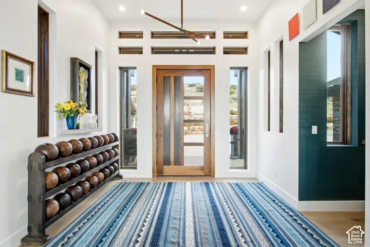 Entryway featuring a wood-framed door with glass panes, high ceilings with a linear modern chandelier, vertical window accents, and wood-finish flooring