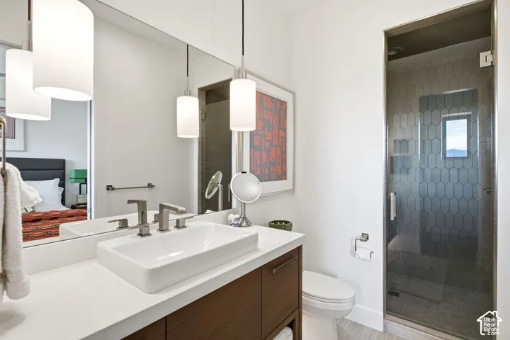 Bathroom featuring a wood-finish vanity with a rectangular vessel sink, solid-surface countertop, dual-tone metal faucet, full-width wall mirror, and a glass-enclosed shower with hexagon-patterned wall tile