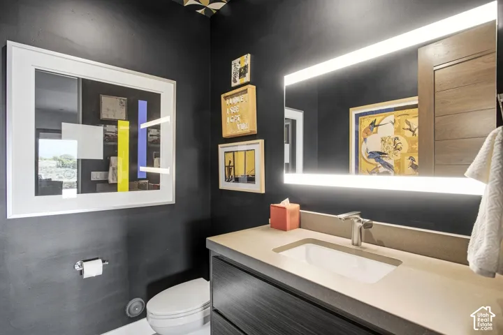 Modern vanity featuring a stone-composite countertop with an integrated rectangular basin, matte-finish cabinetry, a backlit rectangular mirror, and a wall-mounted faucet