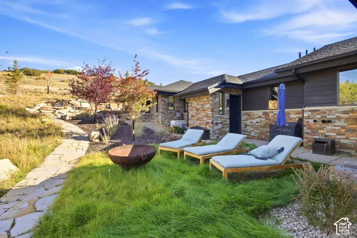 Exterior space featuring natural stone veneer siding, horizontal dark-toned cladding, flagstone walkway, metal fire pit, and terraced landscaping