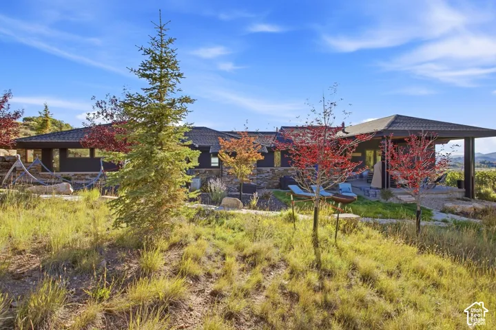 Modern architectural exterior featuring stone veneer siding, a covered concrete patio, multi-hipped rooflines, and mature landscaping