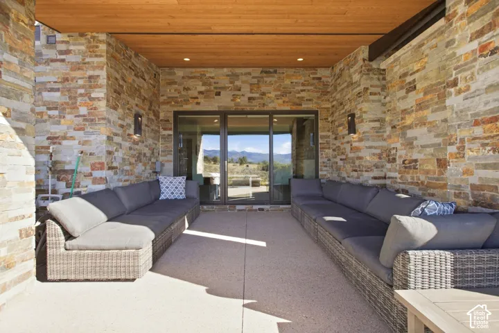 Covered patio featuring natural stone exterior walls, a wood-paneled ceiling with recessed lighting, large glass door system, and a concrete floor