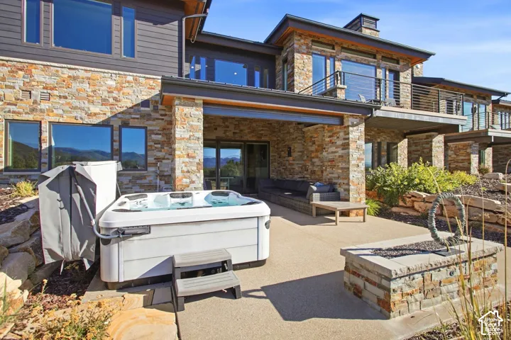 Contemporary residence featuring stacked stone exterior walls, a covered concrete patio, a built-in stone fire pit, and an integrated spa