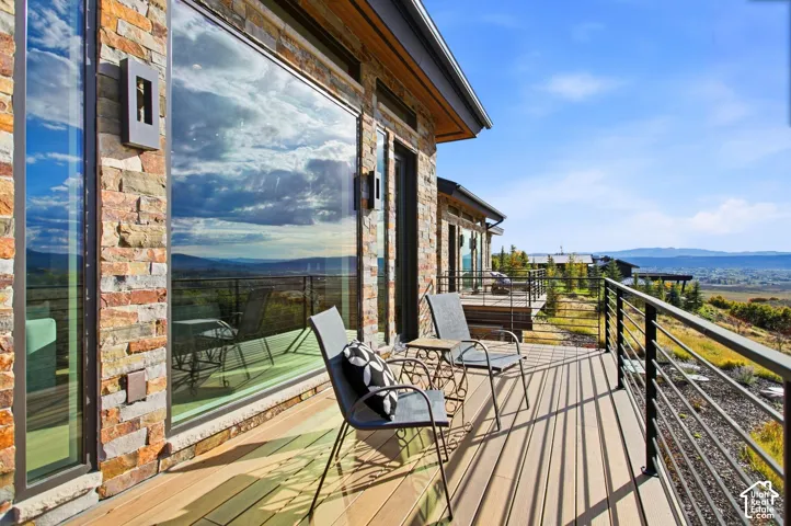 Exterior balcony featuring multi-tonal stacked stone siding, composite decking, metal cable railings, and floor-to-ceiling glass paneling