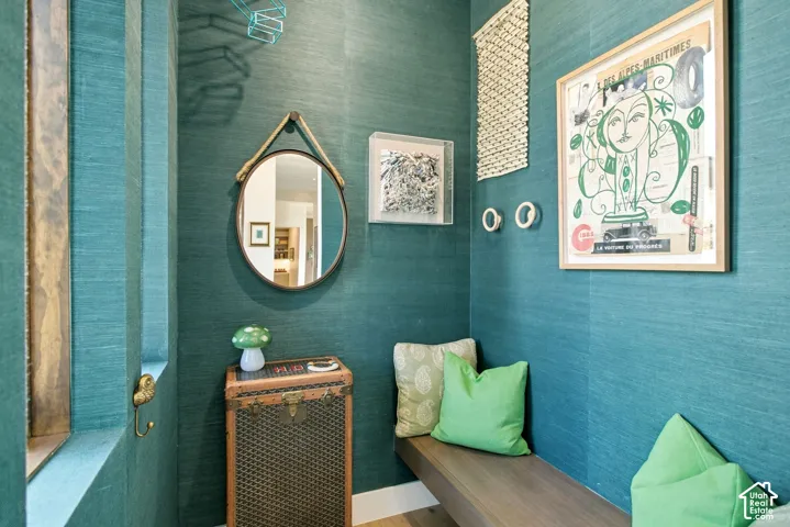 Textured deep-teal wall covering, built-in wooden bench seating, and wall-mounted circular mirror with leather strap detailing