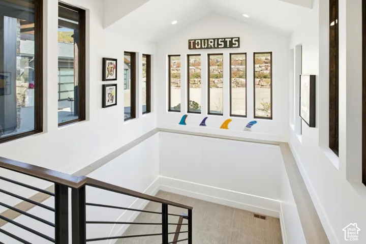 Vaulted ceiling featuring a series of rectangular windows, dark-frame metal staircase railing, and neutral carpeted flooring