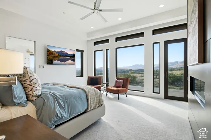 Full-height windows with dark frames, recessed ceiling lighting, brushed metal ceiling fan, fireplace with floor-to-ceiling tile surround, and exterior access via a glass-paneled door