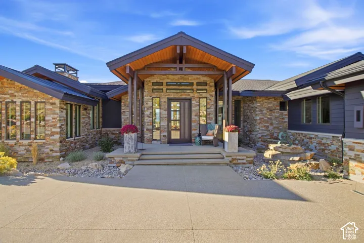 Contemporary exterior featuring multi-textured stone masonry, expansive roof gables with timber framing, an integrated concrete front porch, and tall vertical window panels