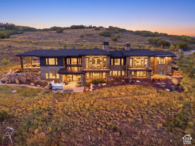 Multi-level exterior featuring natural stone veneer, horizontal metal roof accents, expansive glass windows, integrated covered patio spaces, and a built-in spa