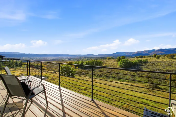 Elevated outdoor deck featuring wood-finish decking and a black metal horizontal cable railing, overlooking expansive mountain and natural landscape scenery