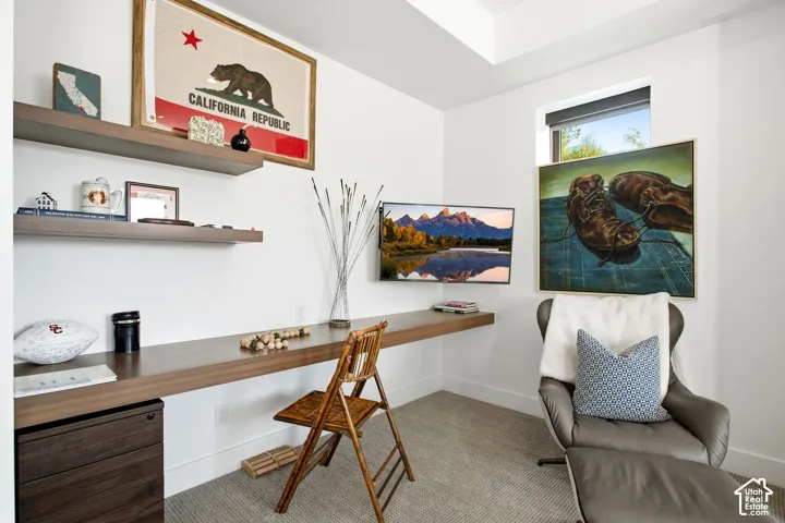 Built-in wall-mounted wood-finish desk, two tiers of floating wood-finish shelving, recessed ceiling detail, and neutral carpet flooring
