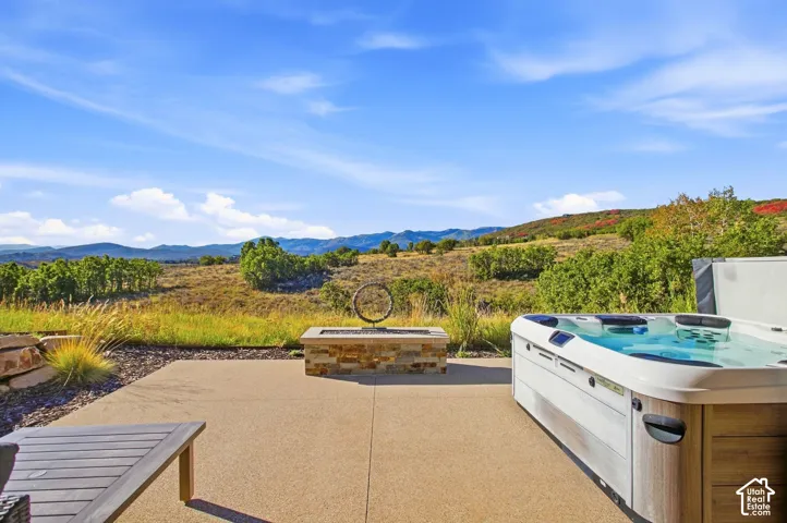 Concrete patio featuring a built-in stone fire pit and a recessed spa, set against a mountainous landscape