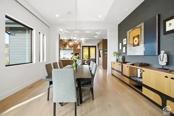 Light-toned wood-finish flooring, recessed lighting, multi-light glass globe chandelier, dark textured accent wall, and built-in wood cabinetry
