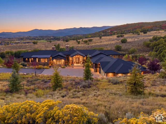 Custom architectural residence featuring stone veneer exterior, expansive metal roofline, multiple chimneys, multi-car garage, and sweeping mountain surroundings