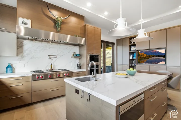 Kitchen featuring wood-finish cabinetry, a large central island with stone-style countertops, professional-grade stainless steel gas range, stone-style full-height backsplash, and built-in double wall ovens