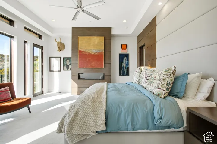 Tray ceiling, floor-to-ceiling accent wall with a linear gas fireplace, integrated ceiling fan, upholstered wall paneling, and expansive glass doors