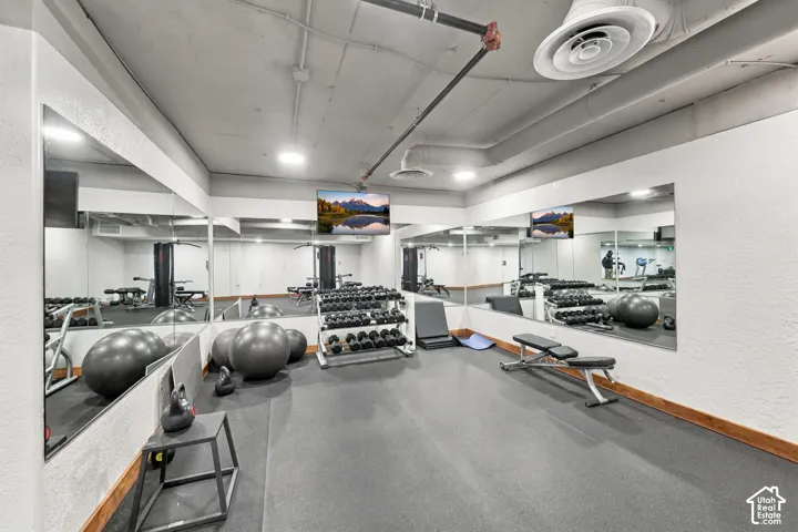 Fitness space featuring industrial-style exposed ceiling, wall-to-wall mirrors, resilient rubber flooring, and recessed lighting