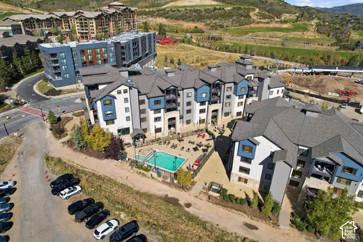 Multi-story residential complex featuring stone and composite siding, shingled roofing, an outdoor swimming pool, and dedicated surface parking