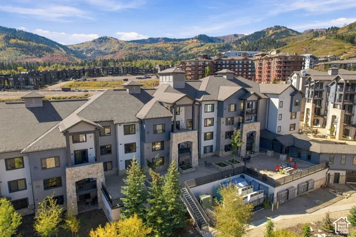 Multi-story building exterior featuring stone and wood siding, covered balconies, a spacious paved patio, and mountain scenery