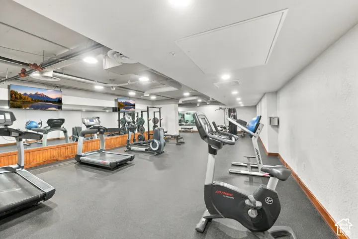 Fitness center featuring gym-grade rubber flooring, wall-to-wall mirror panels, recessed lighting, and wood-finish trim detailing