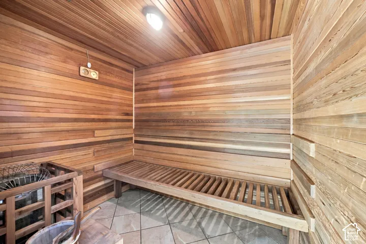 Sauna featuring tongue-and-groove cedar paneling, tiered wooden bench, stone tile flooring, and integrated heating unit