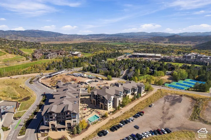 Multi-story residential complex featuring stone and siding exterior, expansive mountain backdrop, on-site outdoor pool, and tennis courts