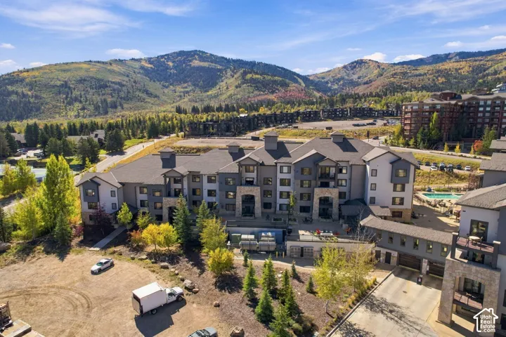 Multi-level structure with stone and stucco exterior, gable rooflines, private balconies, and an outdoor swimming pool against a mountain backdrop