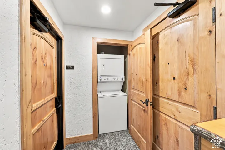 Laundry space featuring a stacked washer and dryer unit, solid wood-finish doors with arched detailing, and matte black hardware