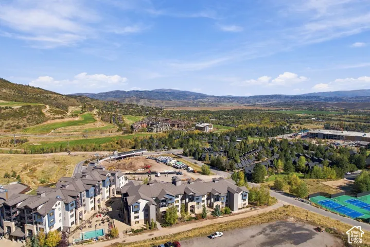 Aerial perspective featuring a multi-story building complex, exterior stone masonry detailing, a paved swimming pool area, and tennis courts set against a mountain backdrop