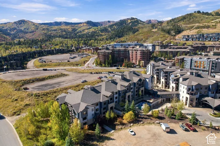 Aerial perspective of a multi-story residential complex featuring stone and siding exterior finishes, complex rooflines, an outdoor pool area, and a mountainous landscape