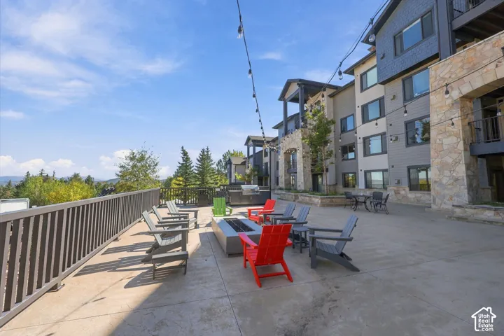 Expansive concrete terrace featuring stone-accented exterior siding, integrated fire pit, metal perimeter railing, and overhead string lighting