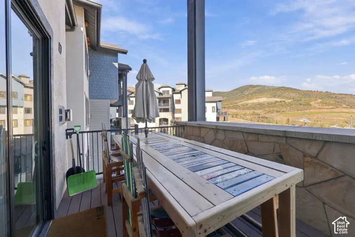Covered balcony featuring composite decking, metal railing, and stone masonry exterior wall with a backdrop of mountainous terrain