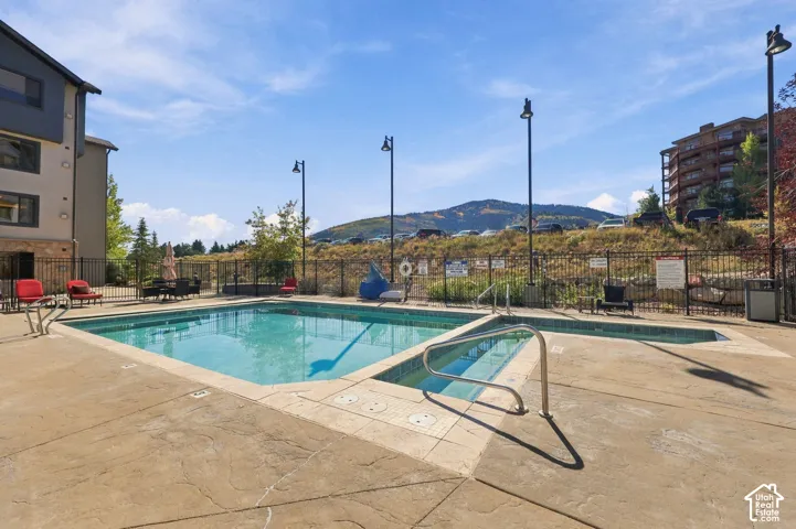 Outdoor swimming pool and attached hot tub with concrete decking, metal perimeter fencing, and mountain backdrop